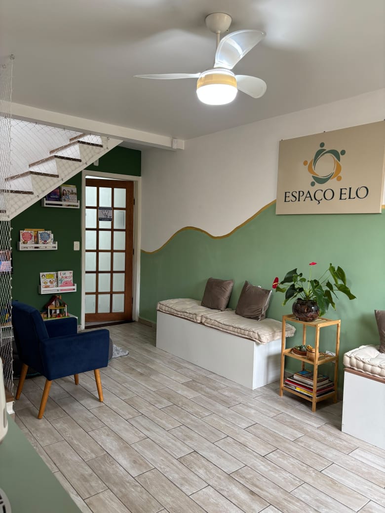 Recepção do Espaço Elo com parede verde-sálvia em onda, bancos com almofadas e a placa da logo