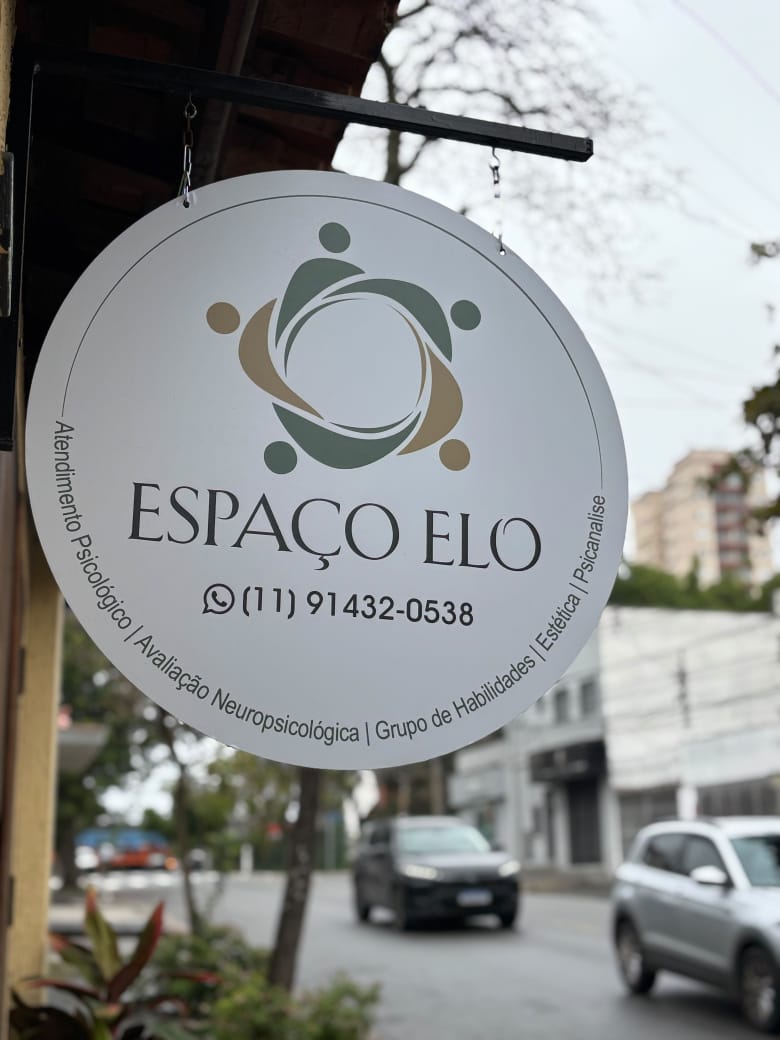 Placa redonda do Espaço Elo na fachada, com a logo e a lista de atendimentos