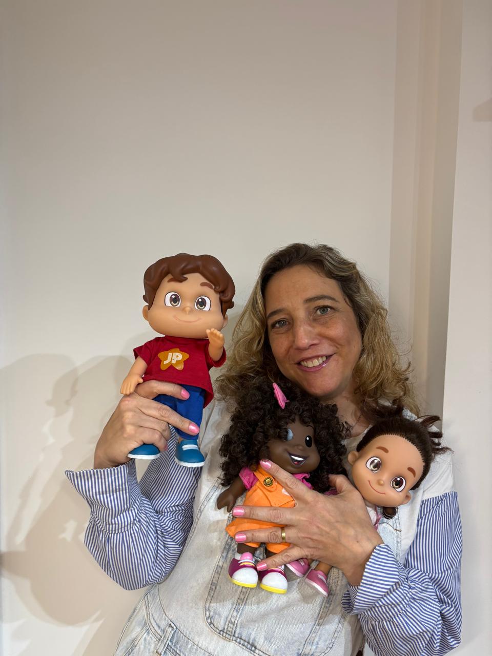 Retrato de Renata Nunes Arruda, psicóloga, sorrindo e segurando bonecos usados nos atendimentos