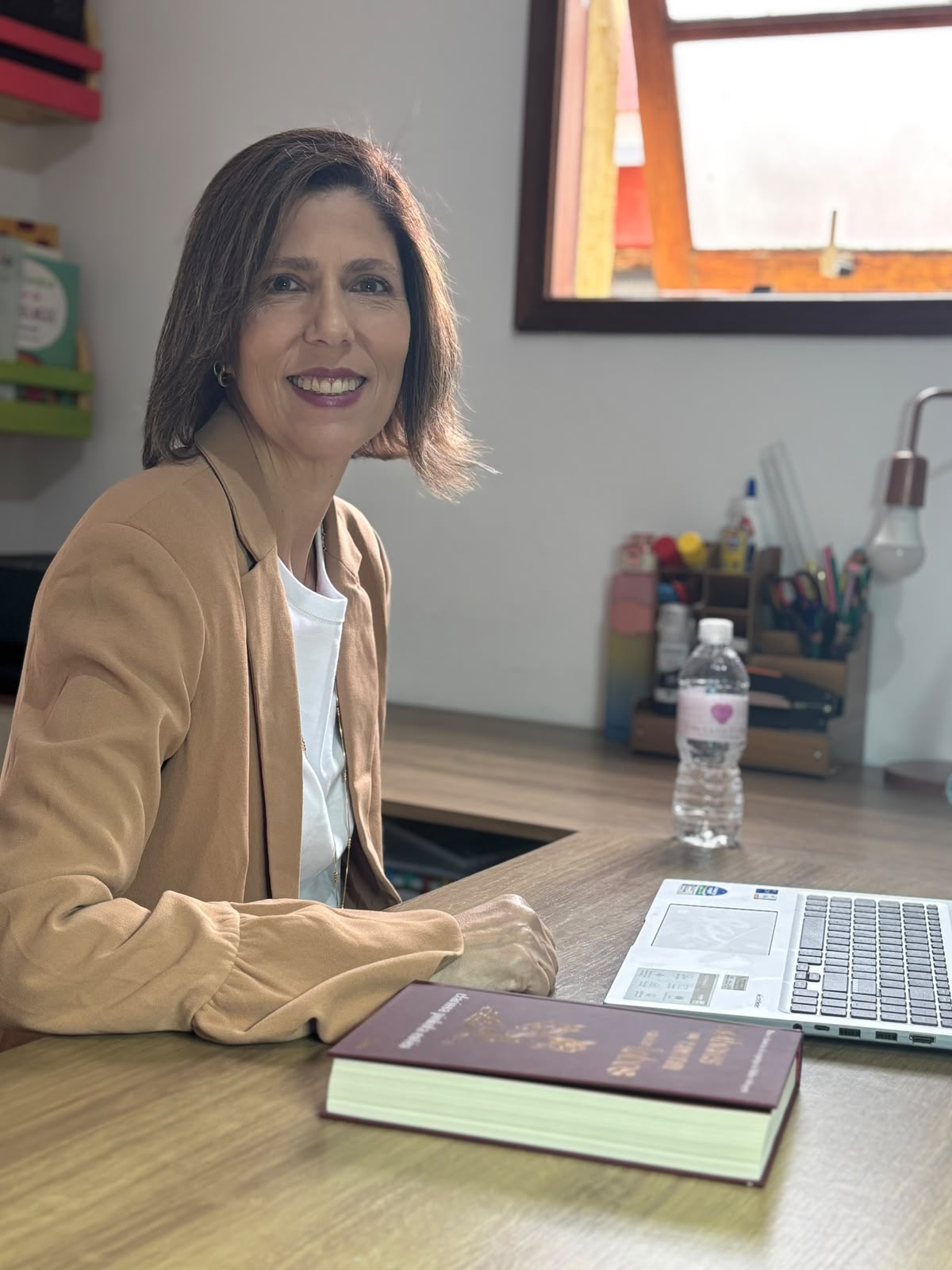 Tatiana sorrindo, sentada à mesa de trabalho com livro e notebook